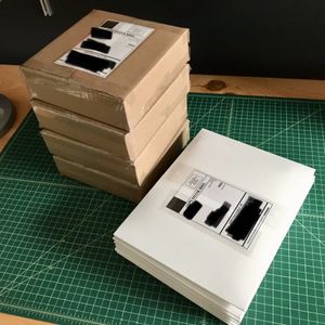 Several small brown cardboard boxes and a stack of white paperboard mailers, all with shipping labels, sit on a green cutting mat on a desktop.