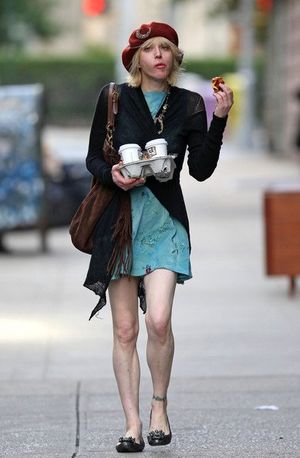 Courtney Love walking on a sidewalk, carrying multiple cups of coffee and munching on a pastry.